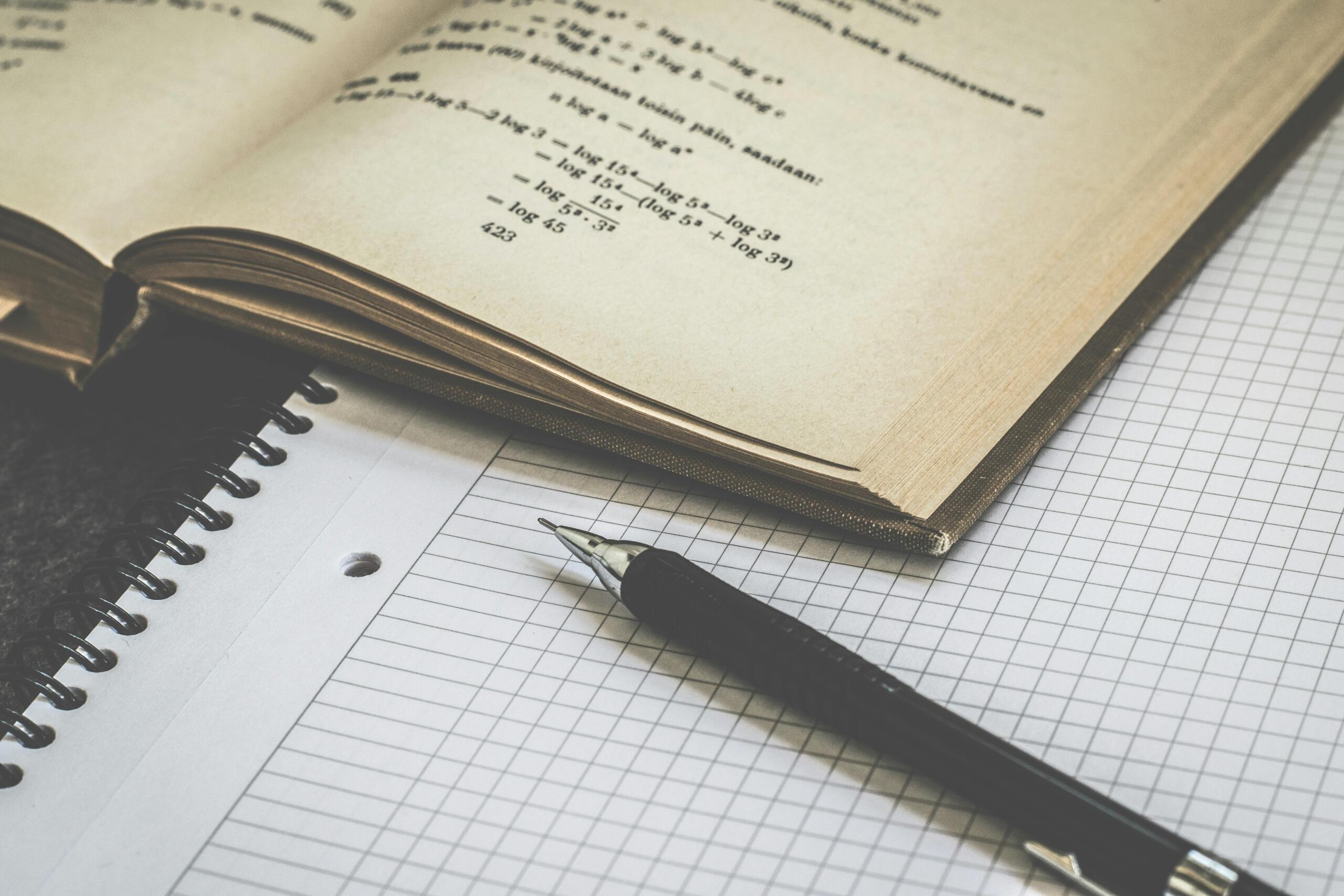 Black click pen resting on white graphing paper with faint grid lines.