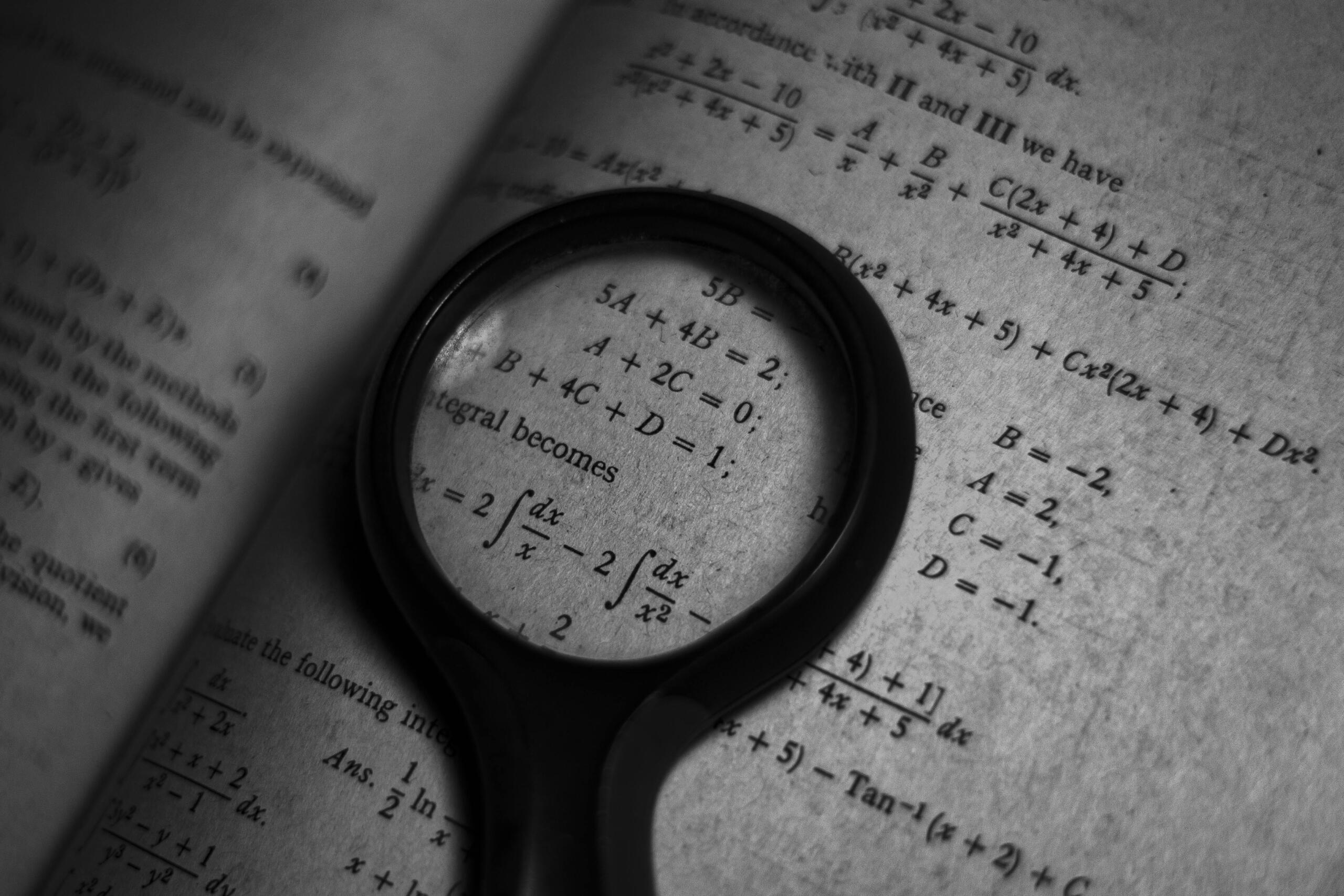 Monochrome photo showing math formulas written on a surface.